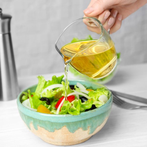 Woman adding tasty apple vinegar into salad with vegetables on table